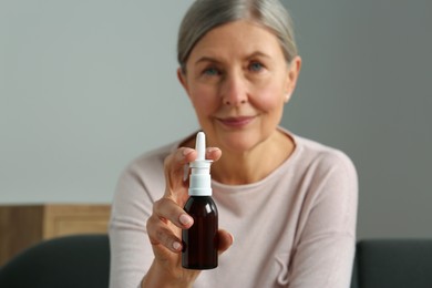 Photo of Woman holding nasal spray indoors, focus on bottle