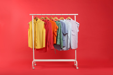 Photo of Bright clothes hanging on rack against red background. Rainbow colors