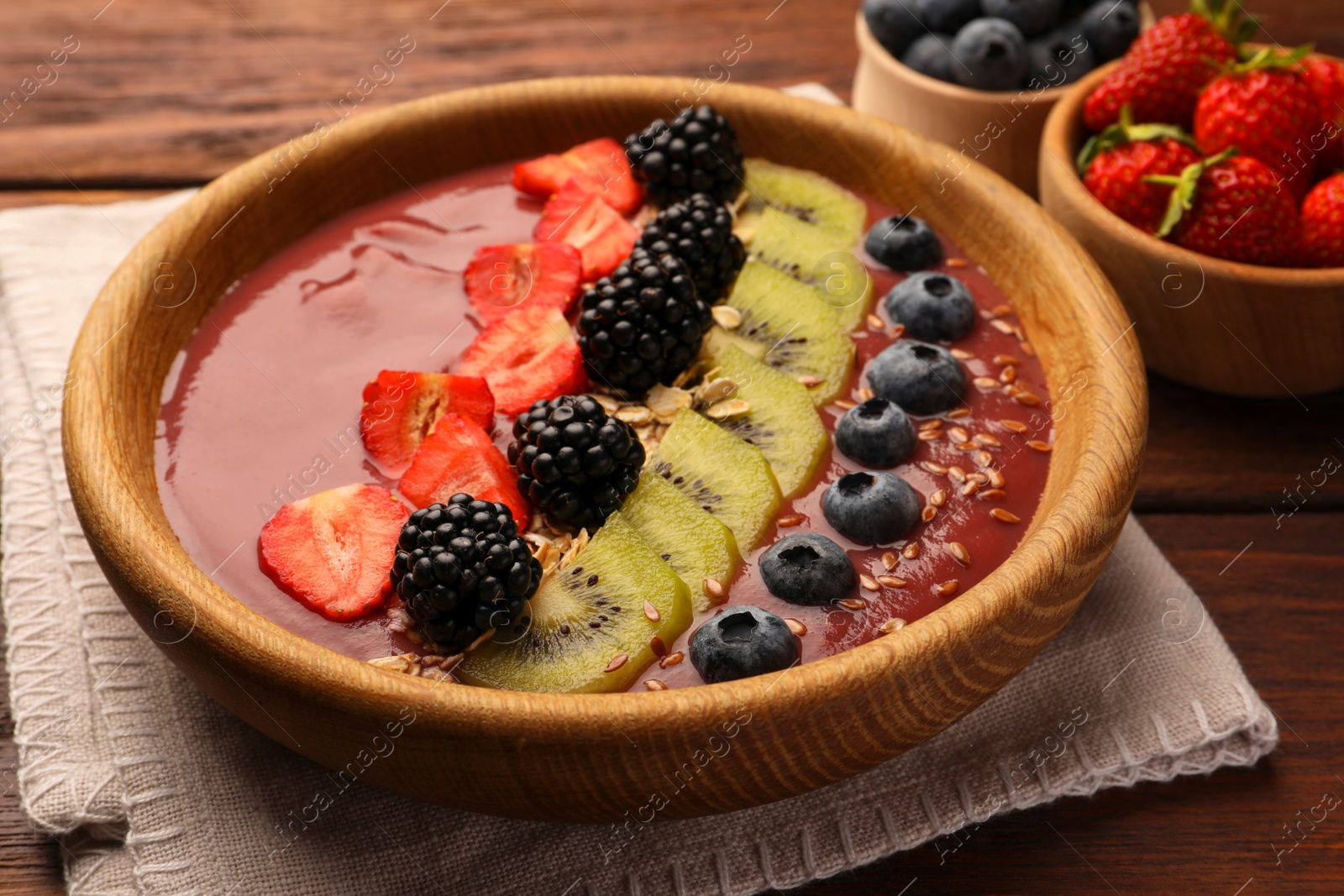 Photo of Bowl of delicious smoothie with fresh blueberries, strawberries, kiwi slices and blackberries on wooden table, closeup