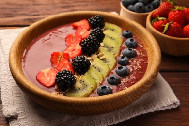 Bowl of delicious smoothie with fresh blueberries, strawberries, kiwi slices and blackberries on wooden table, closeup