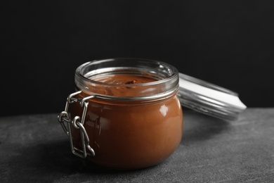 Jar with tasty chocolate cream on table against dark background