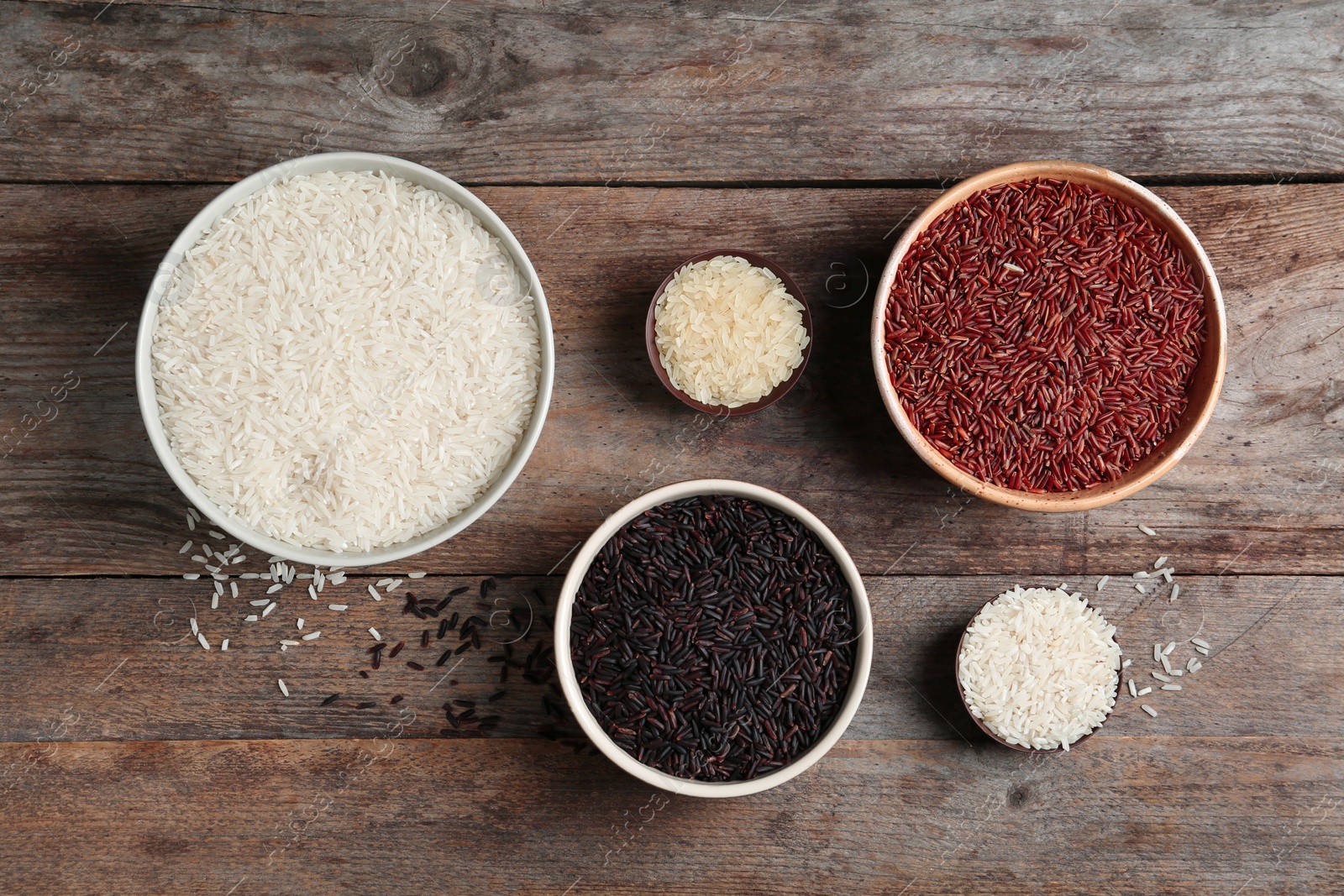 Photo of Flat lay composition with brown and other types of rice in bowls on wooden background