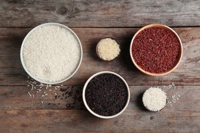 Flat lay composition with brown and other types of rice in bowls on wooden background