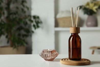 Aromatic reed air freshener and candle on white table in room. Space for text