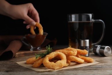Photo of Pile of delicious crunchy fried onion rings and rosemary on wooden table