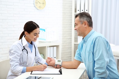 Doctor checking mature man's pulse with medical device in hospital