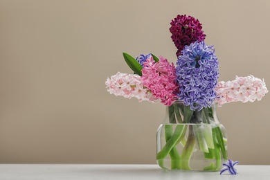 Photo of Beautiful hyacinths in glass vase on table against color background, space for text. Spring flowers