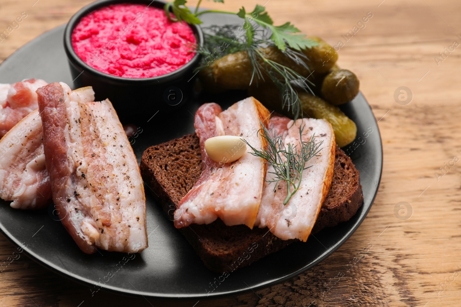 Photo of Pork fatback with rye bread and ingredients on wooden table, closeup