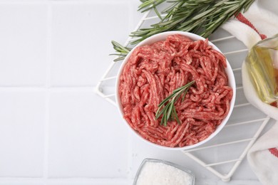 Photo of Flat lay composition with fresh raw ground meat and rosemary in bowl on white tiled table. Space for text