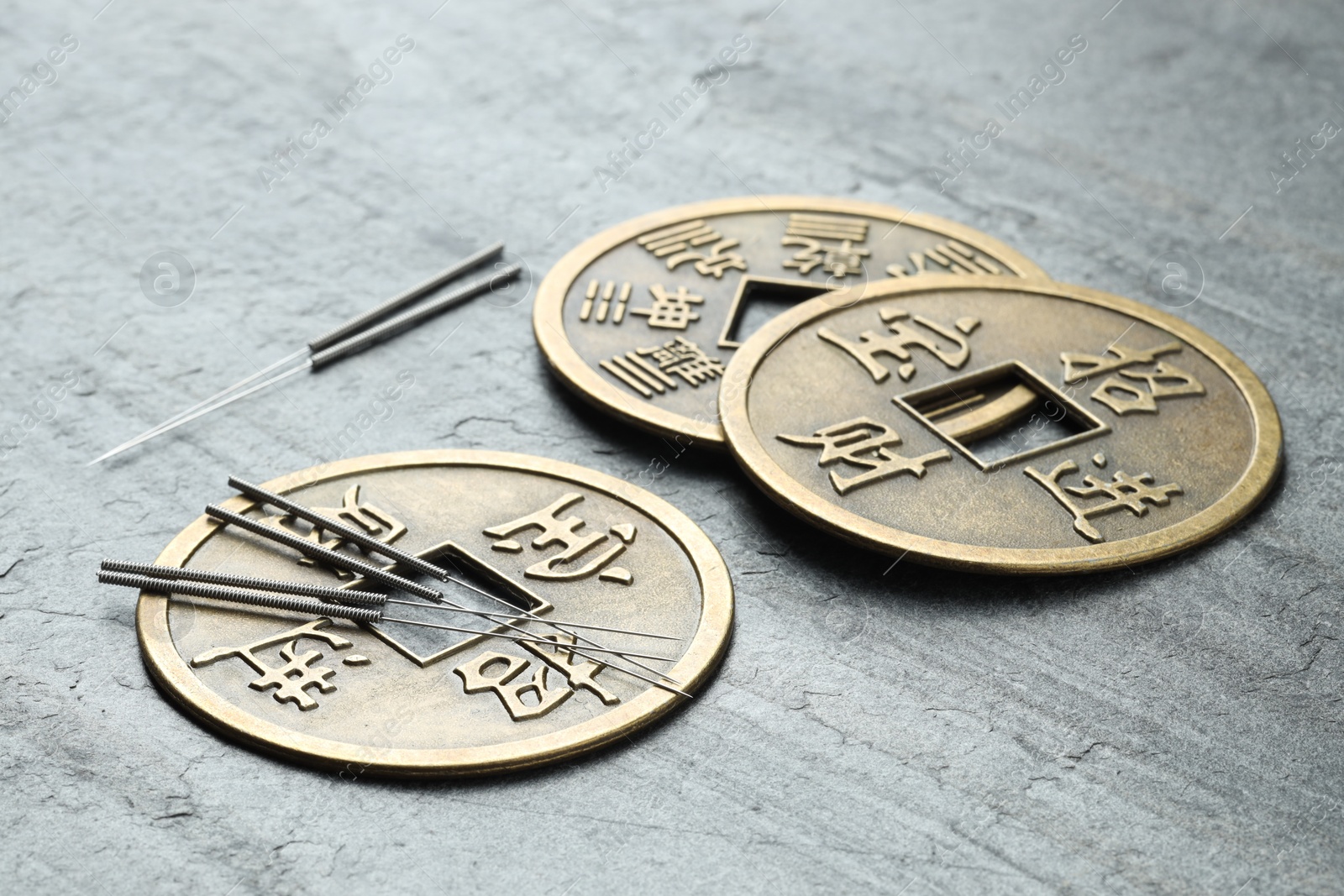 Photo of Acupuncture needles and Chinese coins on grey textured table, closeup