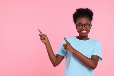 Photo of Happy young woman pointing at something on pink background. Space for text