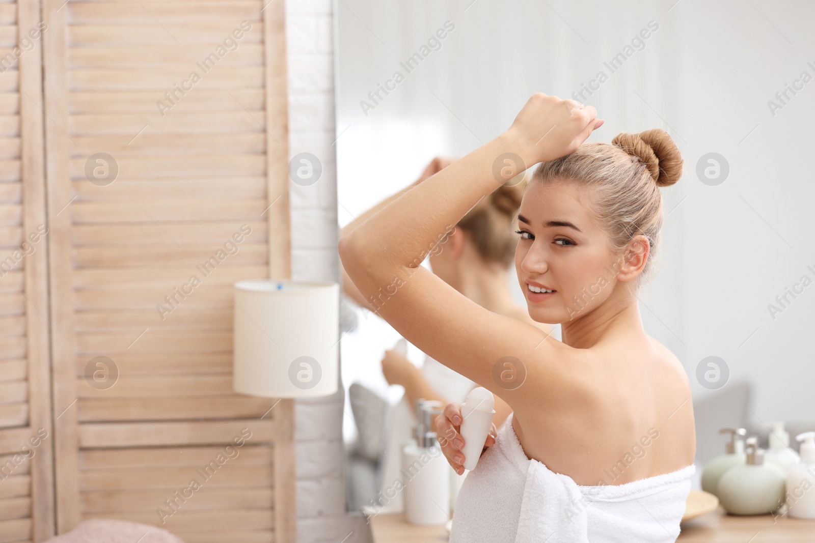 Photo of Beautiful young woman applying deodorant after shower in bathroom