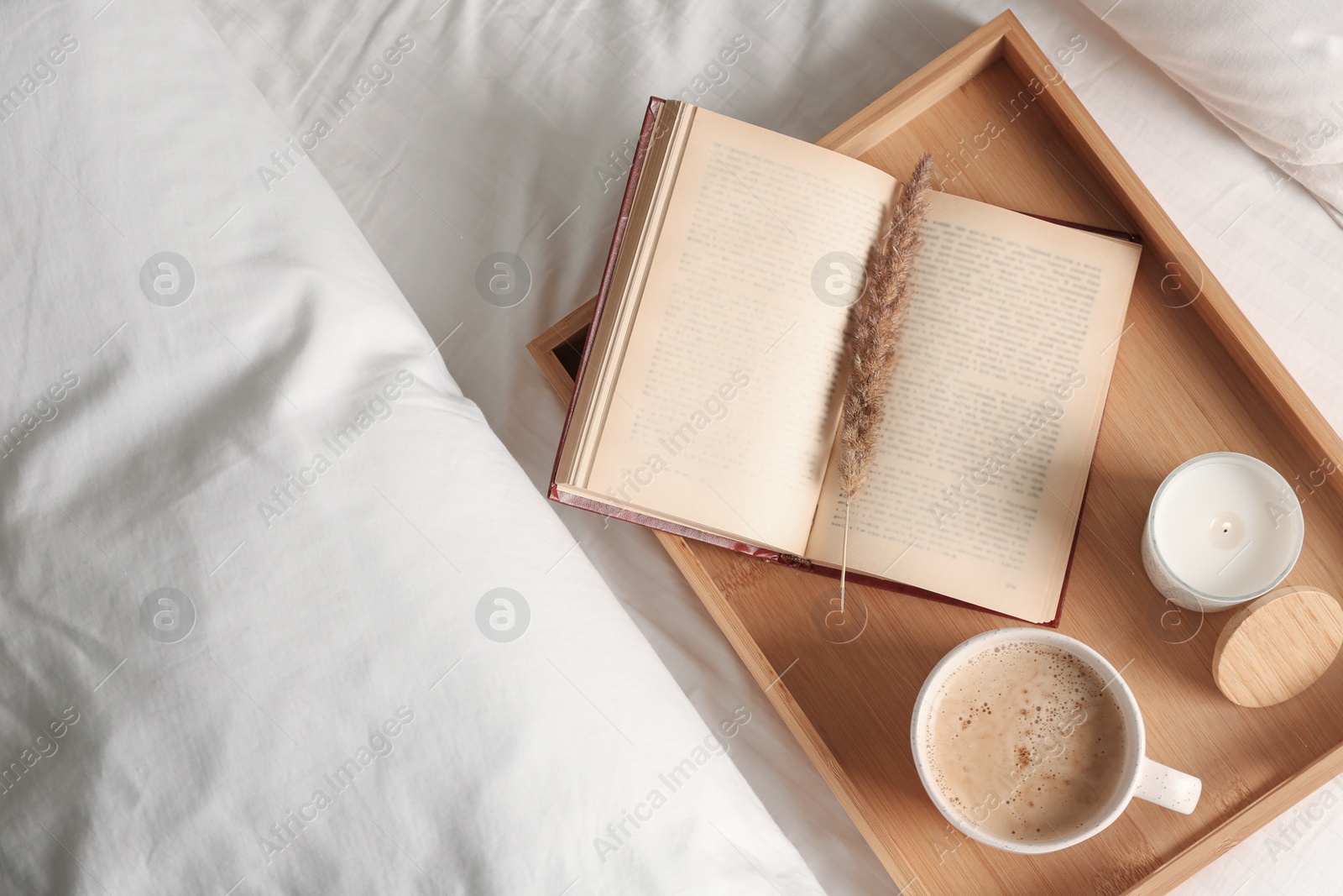 Photo of Cup of aromatic coffee, book and candle on bed with soft blanket indoors, top view