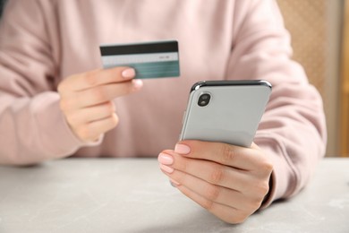 Photo of Online payment. Woman using credit card and smartphone at light grey table indoors, closeup