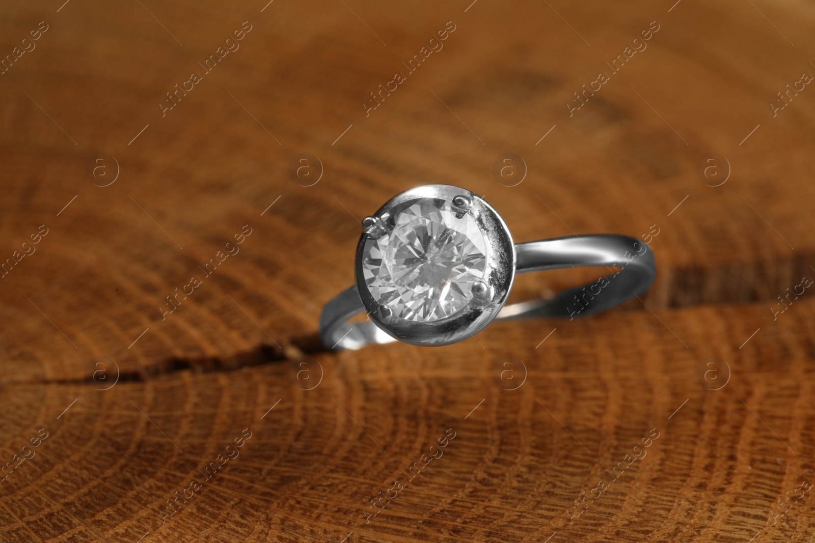 Photo of Beautiful luxury engagement ring with gemstone on tree stump, closeup