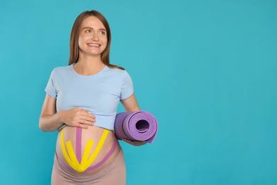 Photo of Beautiful pregnant woman with kinesio tapes holding sport mat on light blue background. Space for text