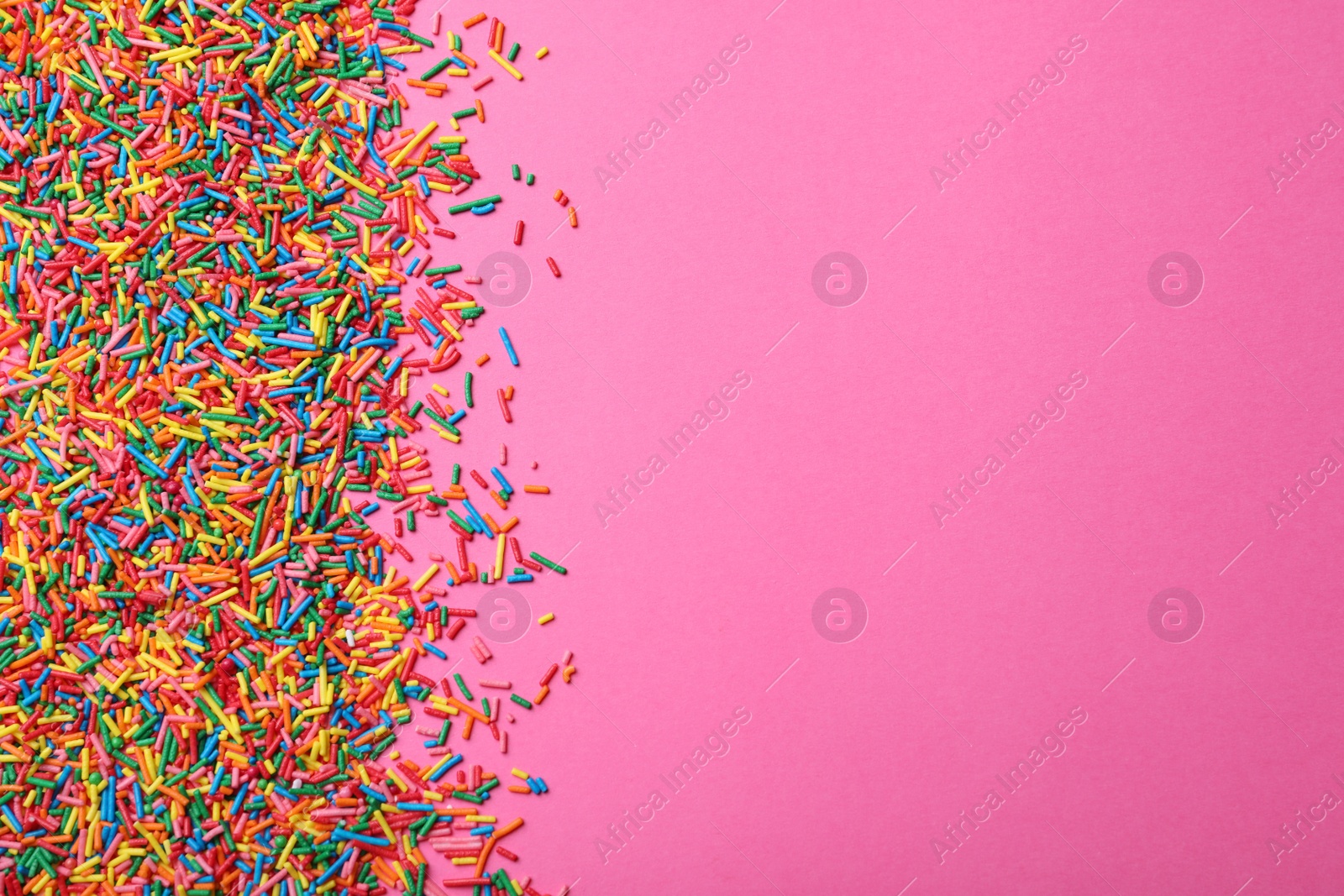 Photo of Bright colorful sprinkles on pink background, flat lay with space for text. Confectionery decor