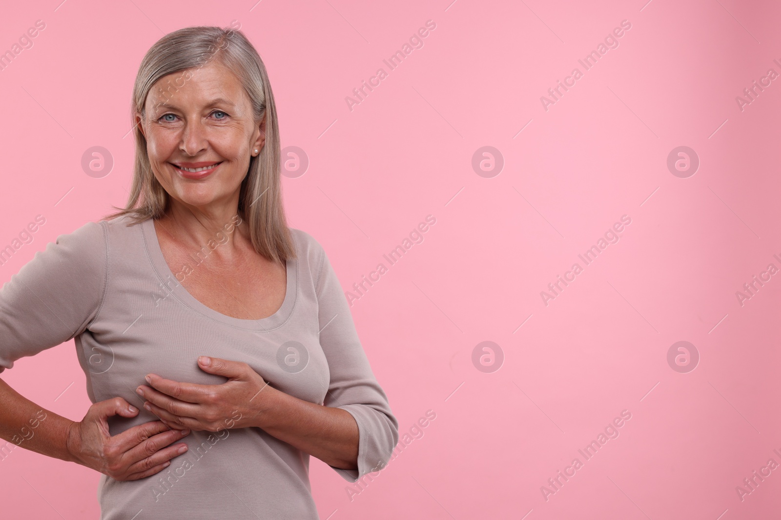 Photo of Beautiful senior woman doing breast self-examination on pink background, space for text