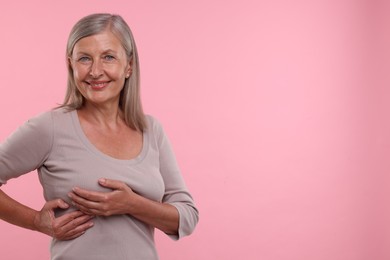 Beautiful senior woman doing breast self-examination on pink background, space for text