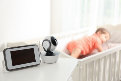 Photo of Baby monitor and camera on table near crib with child in room. Video nanny