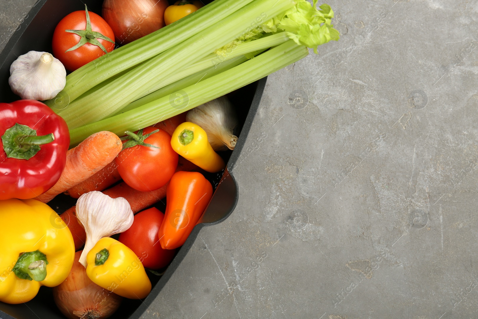 Photo of Black pot with fresh vegetables on grey table, top view. Space for text