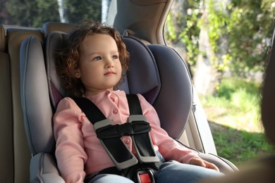 Cute little girl sitting in child safety seat inside car