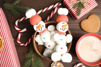 Flat lay composition with funny snowmen made of marshmallows in bowl on wooden table