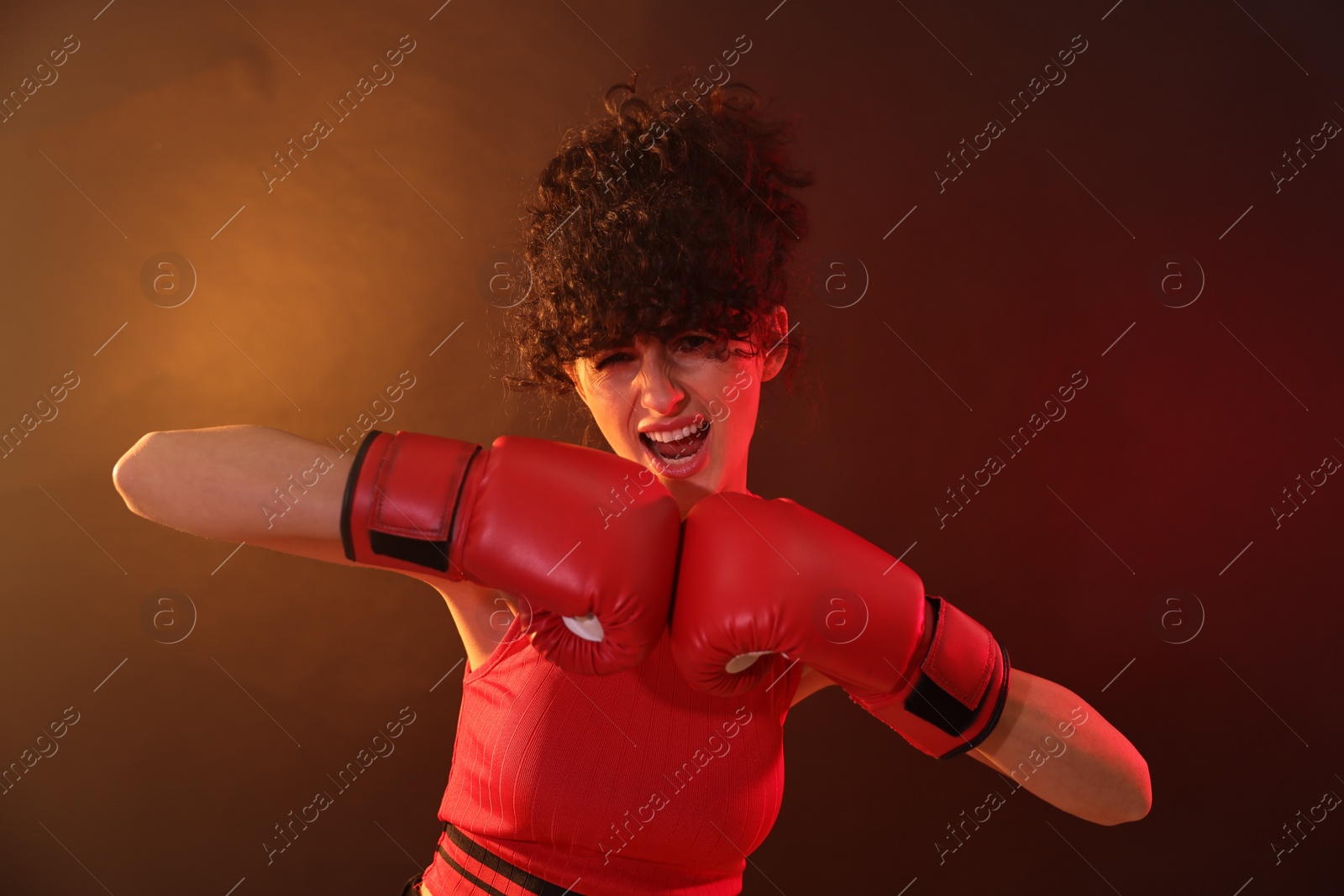 Photo of Beautiful young woman with boxing gloves on color background in neon lights