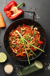 Photo of Shrimp stir fry with vegetables in wok and ingredients on black table, flat lay
