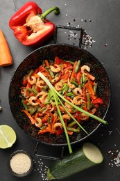 Shrimp stir fry with vegetables in wok and ingredients on black table, flat lay