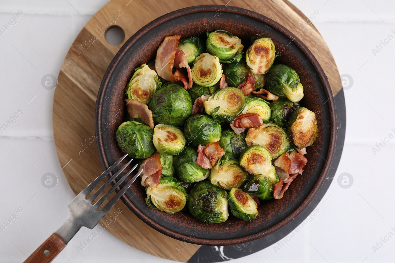 Photo of Delicious roasted Brussels sprouts and bacon in bowl on white table, top view