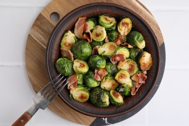 Delicious roasted Brussels sprouts and bacon in bowl on white table, top view