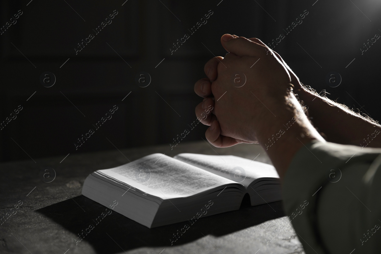 Photo of Religion. Christian man praying over Bible at table, closeup. Space for text