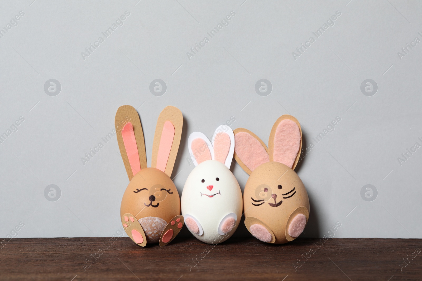 Photo of Eggs as cute bunnies on wooden table against light grey background, space for text. Easter celebration