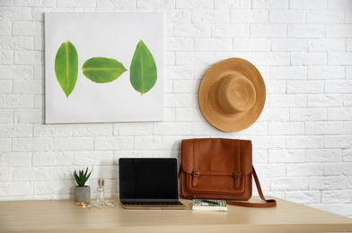 Photo of Stylish workplace with modern laptop on table near brick wall. Fashion blogger