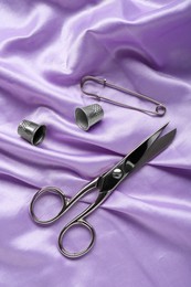 Photo of Silver thimbles and other sewing accessories on purple cloth, flat lay