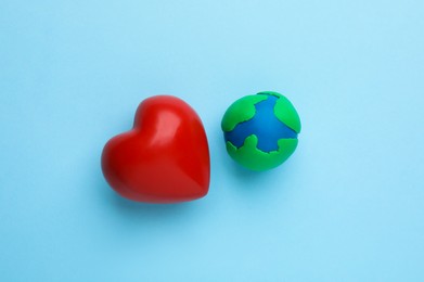 Photo of Plasticine model of planet and red heart on light blue background, flat lay. Earth Day