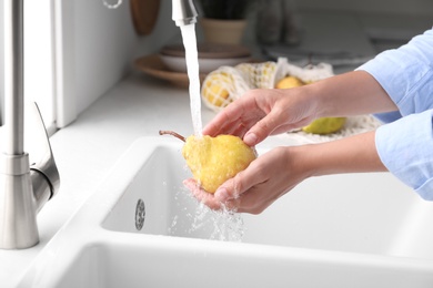 Woman washing fresh ripe pear in kitchen, closeup