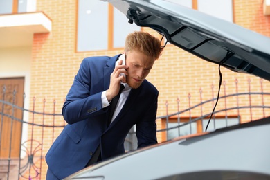 Photo of troubled young businessman talking on phone near broken car outdoors