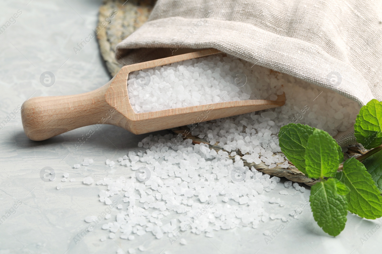 Photo of Wooden scoop with natural sea salt, sack and mint on light grey marble table, closeup