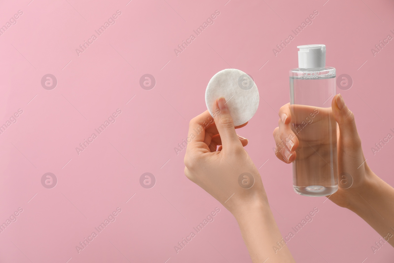 Photo of Woman holding makeup remover and cotton pad on pink background, closeup. Space for text