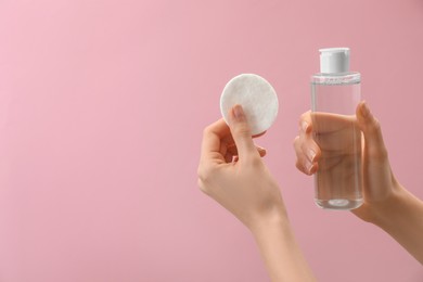 Woman holding makeup remover and cotton pad on pink background, closeup. Space for text