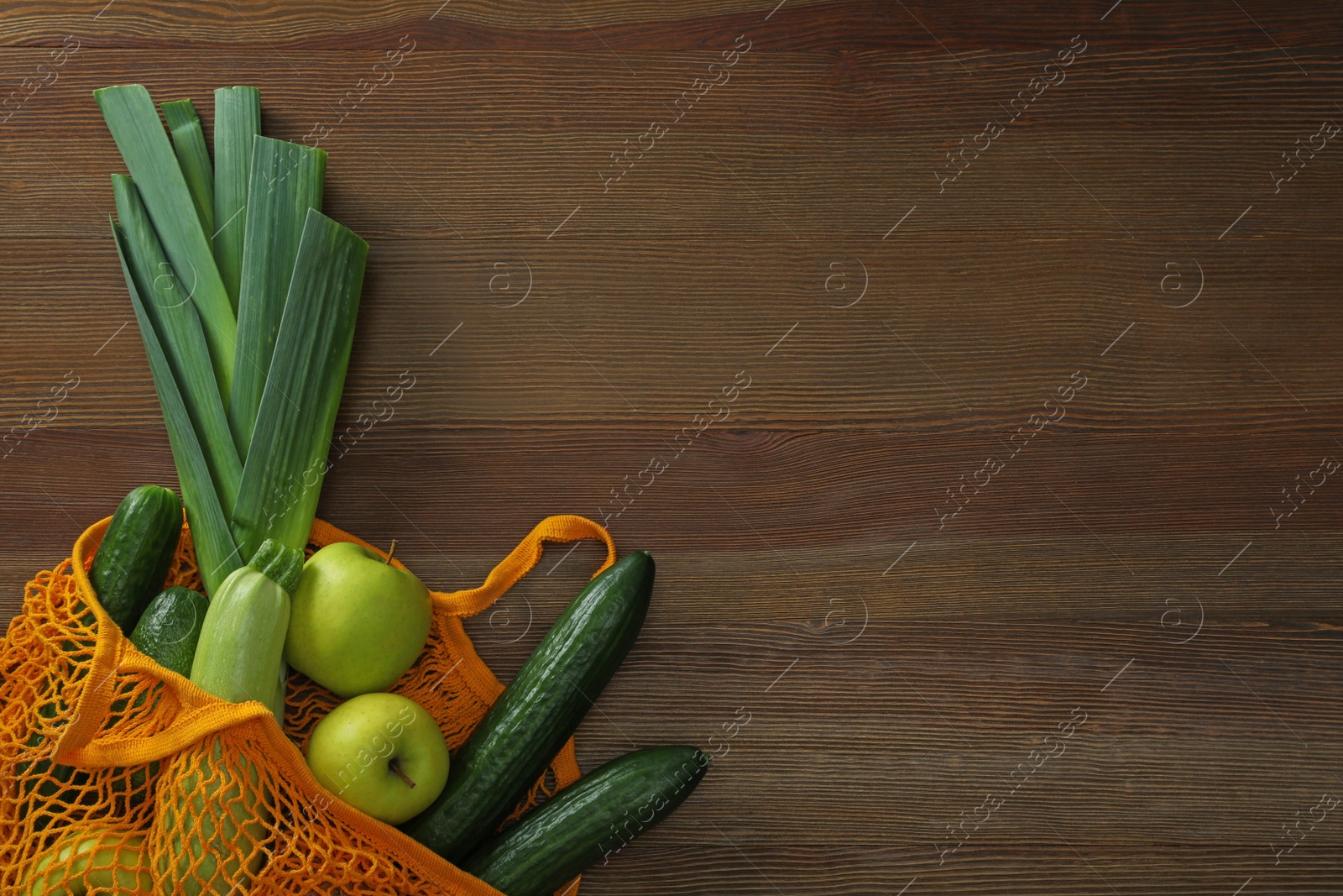 Photo of Net bag with vegetables and fruits on wooden table, top view. Space for text