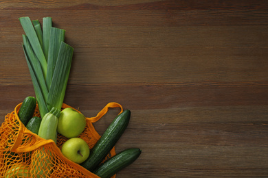 Net bag with vegetables and fruits on wooden table, top view. Space for text