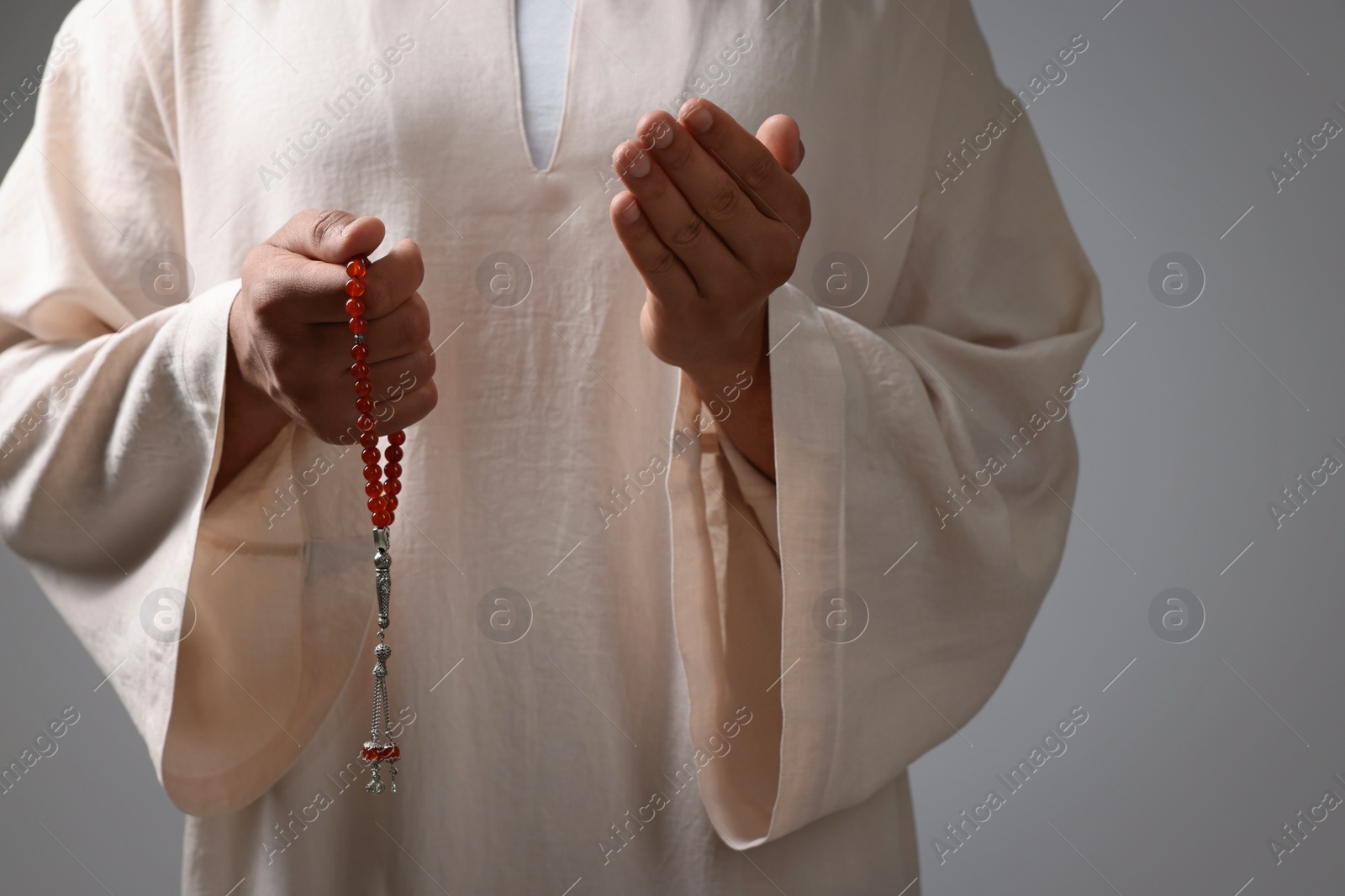 Photo of Muslim man with misbaha praying on light grey background, closeup