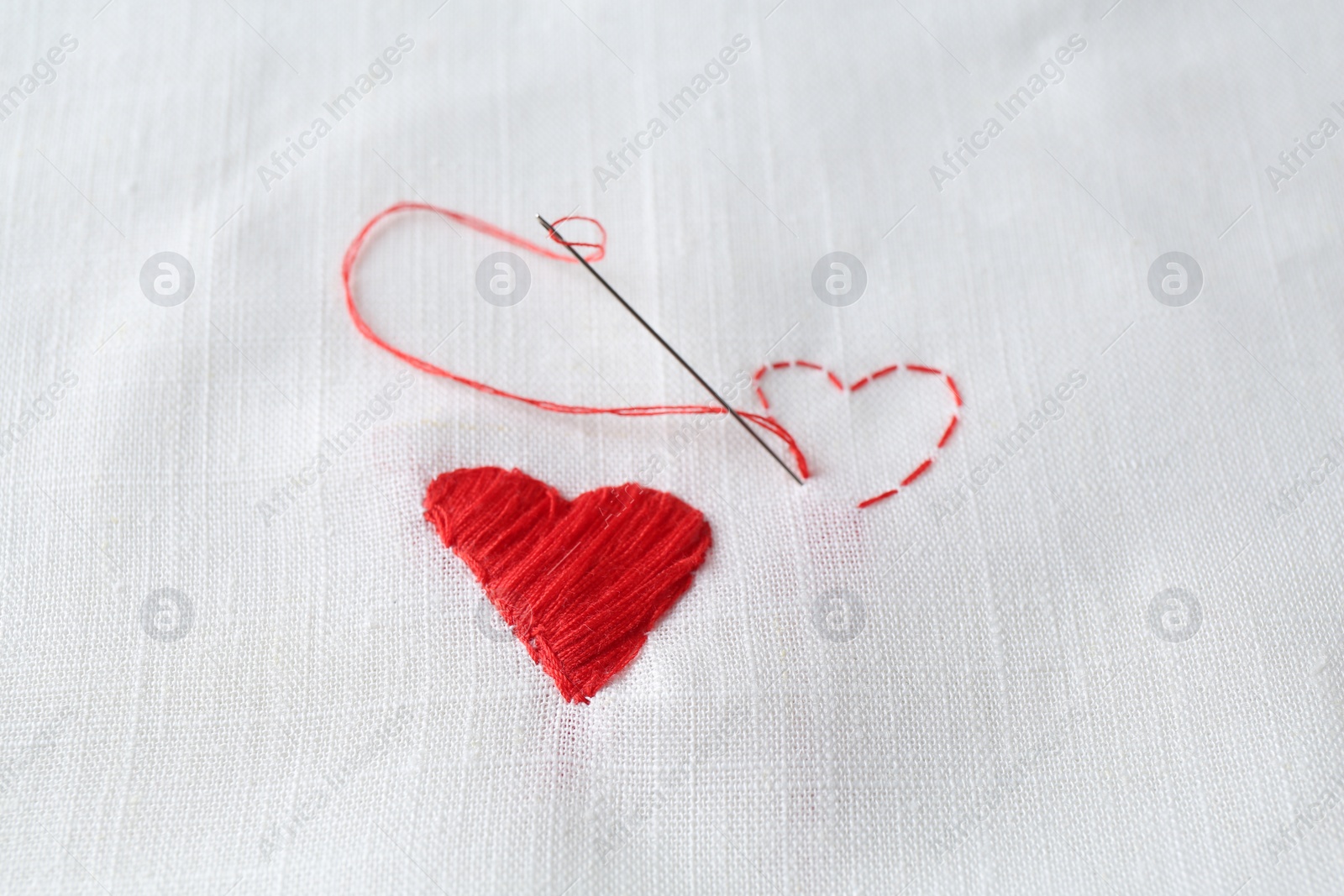 Photo of Embroidered red heart and needle on white cloth, closeup