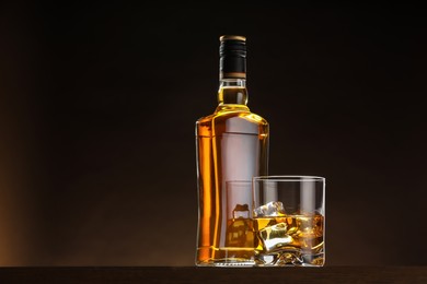 Photo of Whiskey with ice cubes in glass and bottle on table, space for text