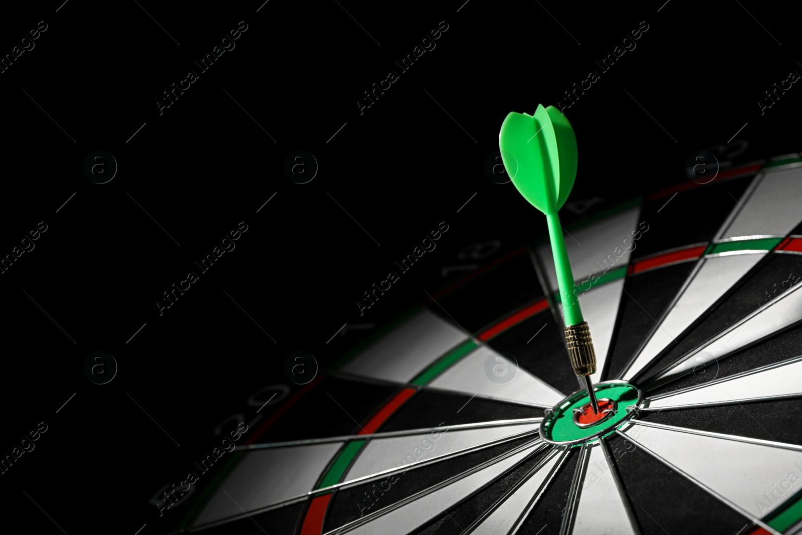 Photo of Green arrow hitting target on dart board against black background. Space for text