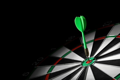 Green arrow hitting target on dart board against black background. Space for text