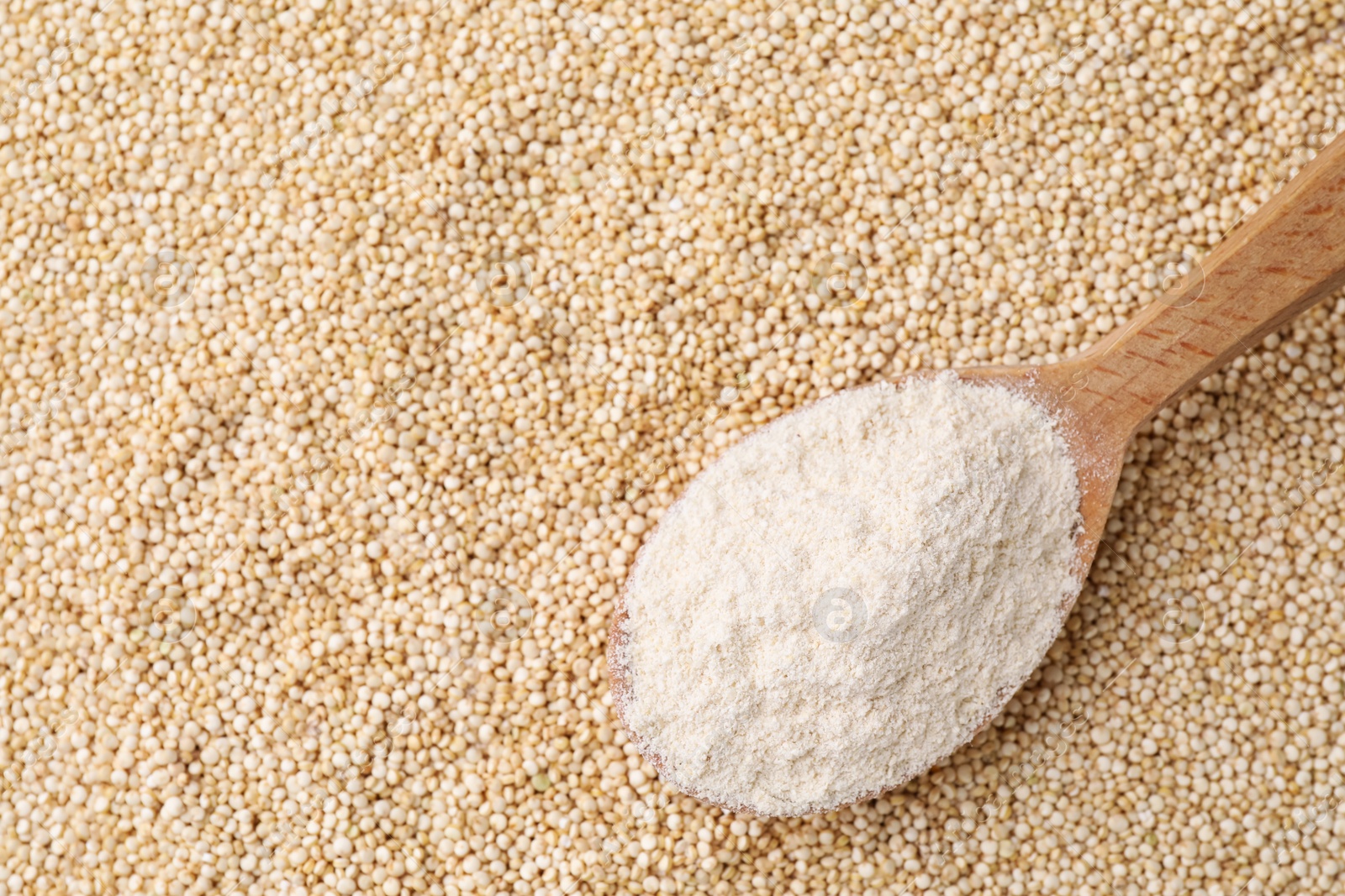 Photo of Wooden spoon with fresh quinoa flour on seeds, top view. Space for text